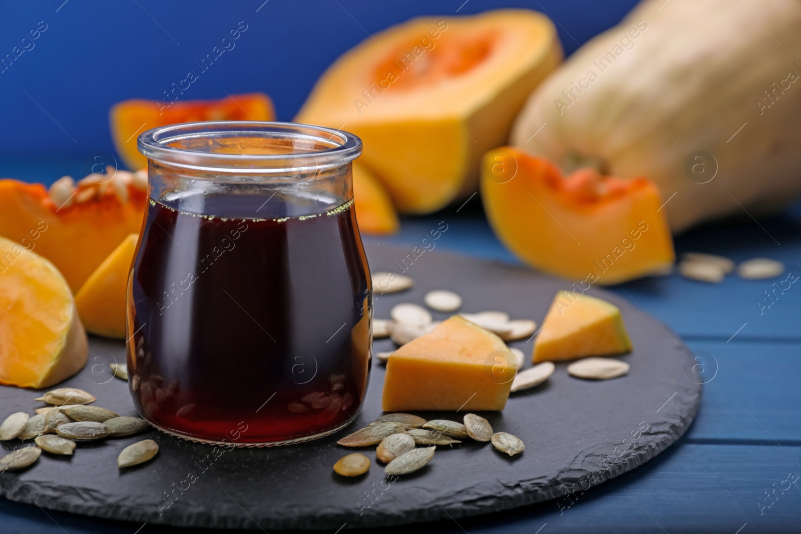 Photo of Fresh pumpkin seed oil in glass jar on blue wooden table. Space for text