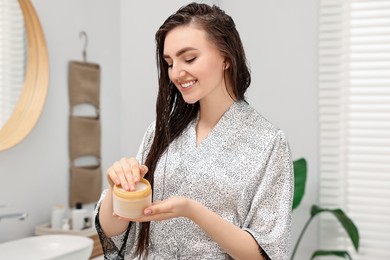 Photo of Young woman with jar of hair mask in bathroom