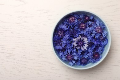 Photo of Beautiful colorful cornflowers in bowl on white wooden table, top view. Space for text
