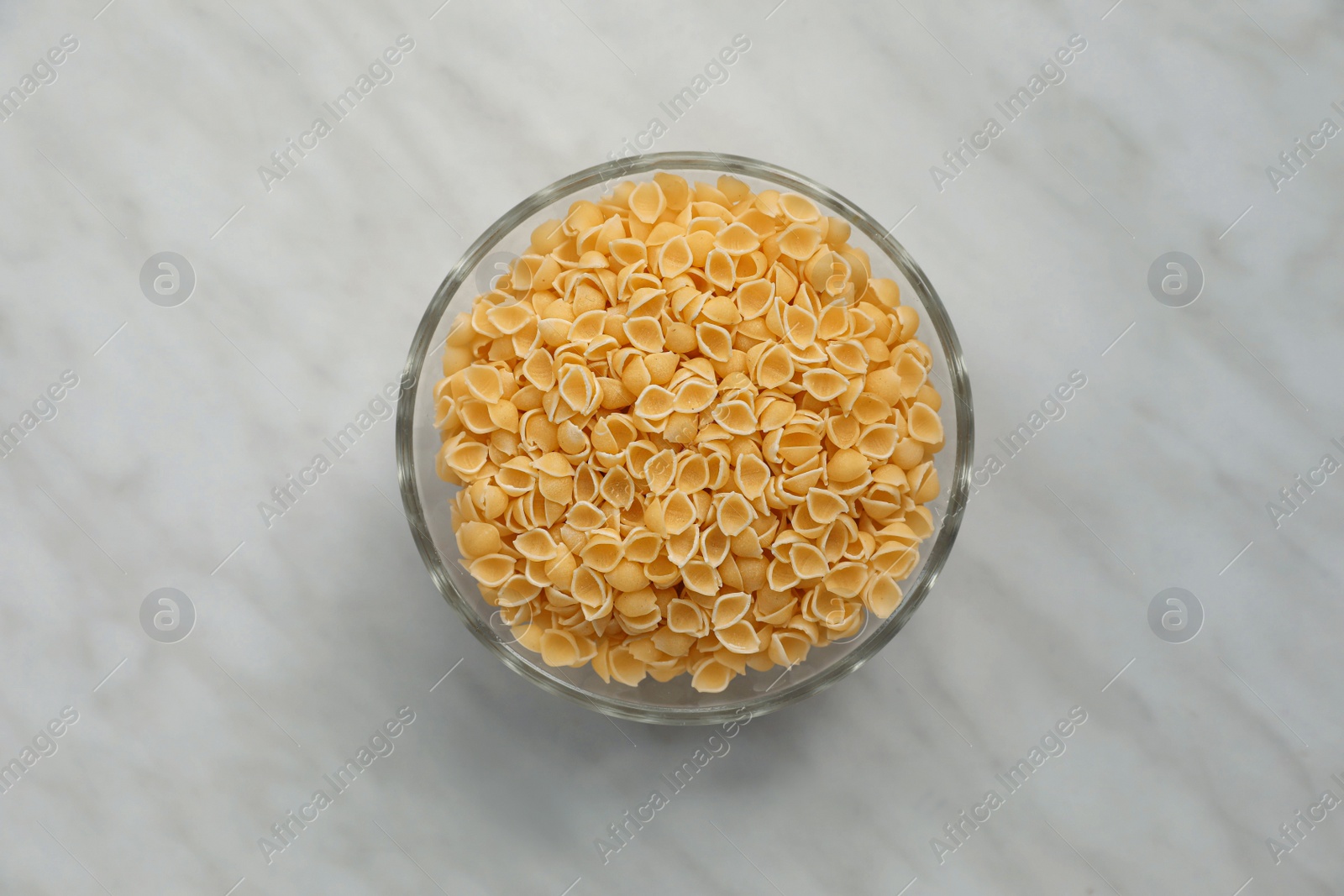 Photo of Bowl with uncooked conchiglie pasta on white marble table, top view