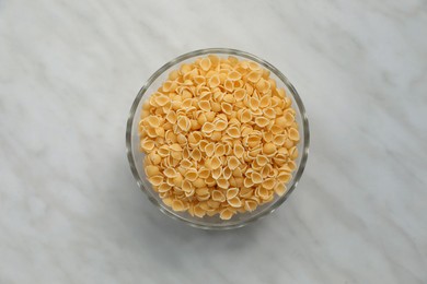 Photo of Bowl with uncooked conchiglie pasta on white marble table, top view