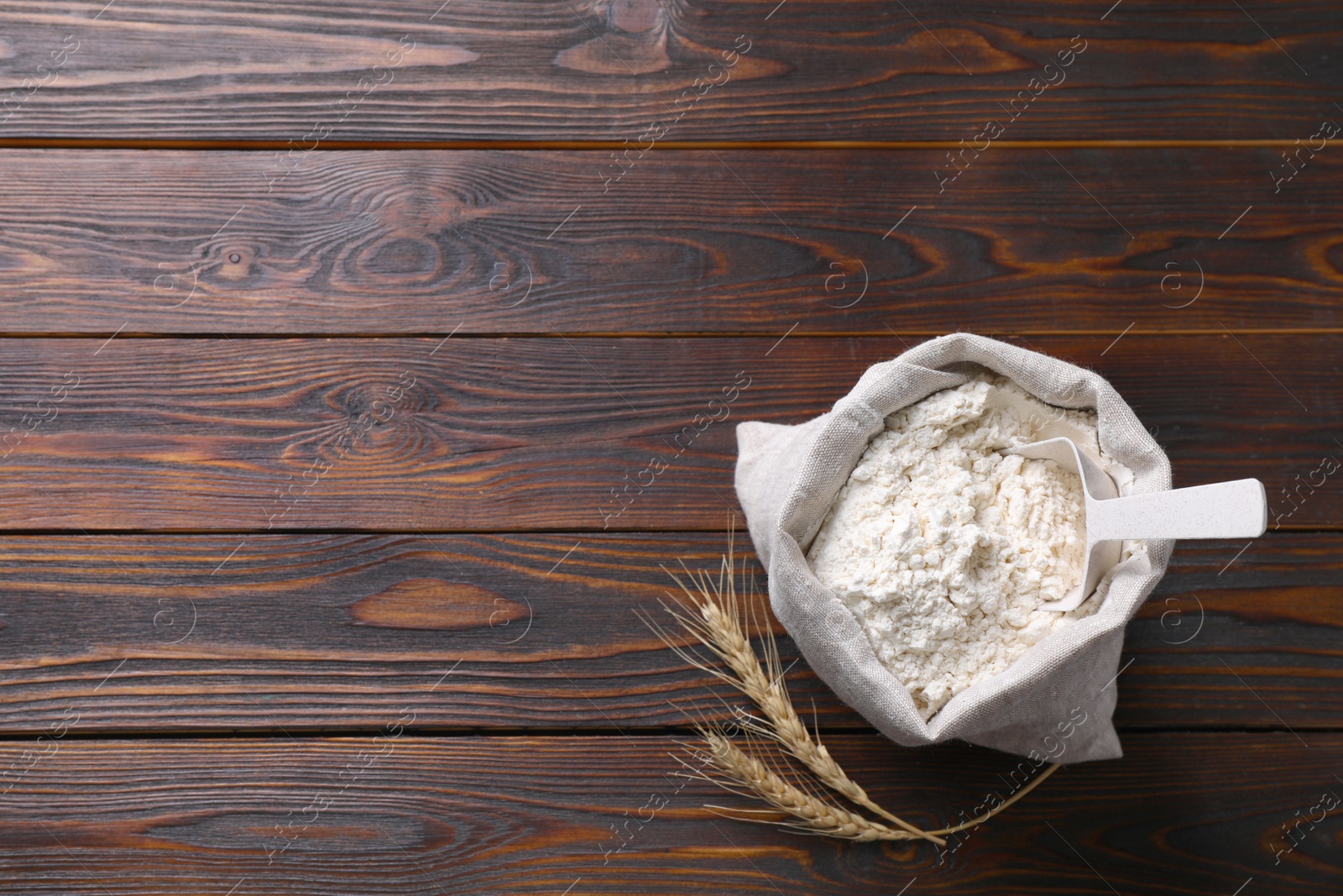 Photo of Sack with flour and wheat spikes on wooden background, flat lay. Space for text