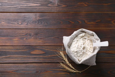 Photo of Sack with flour and wheat spikes on wooden background, flat lay. Space for text