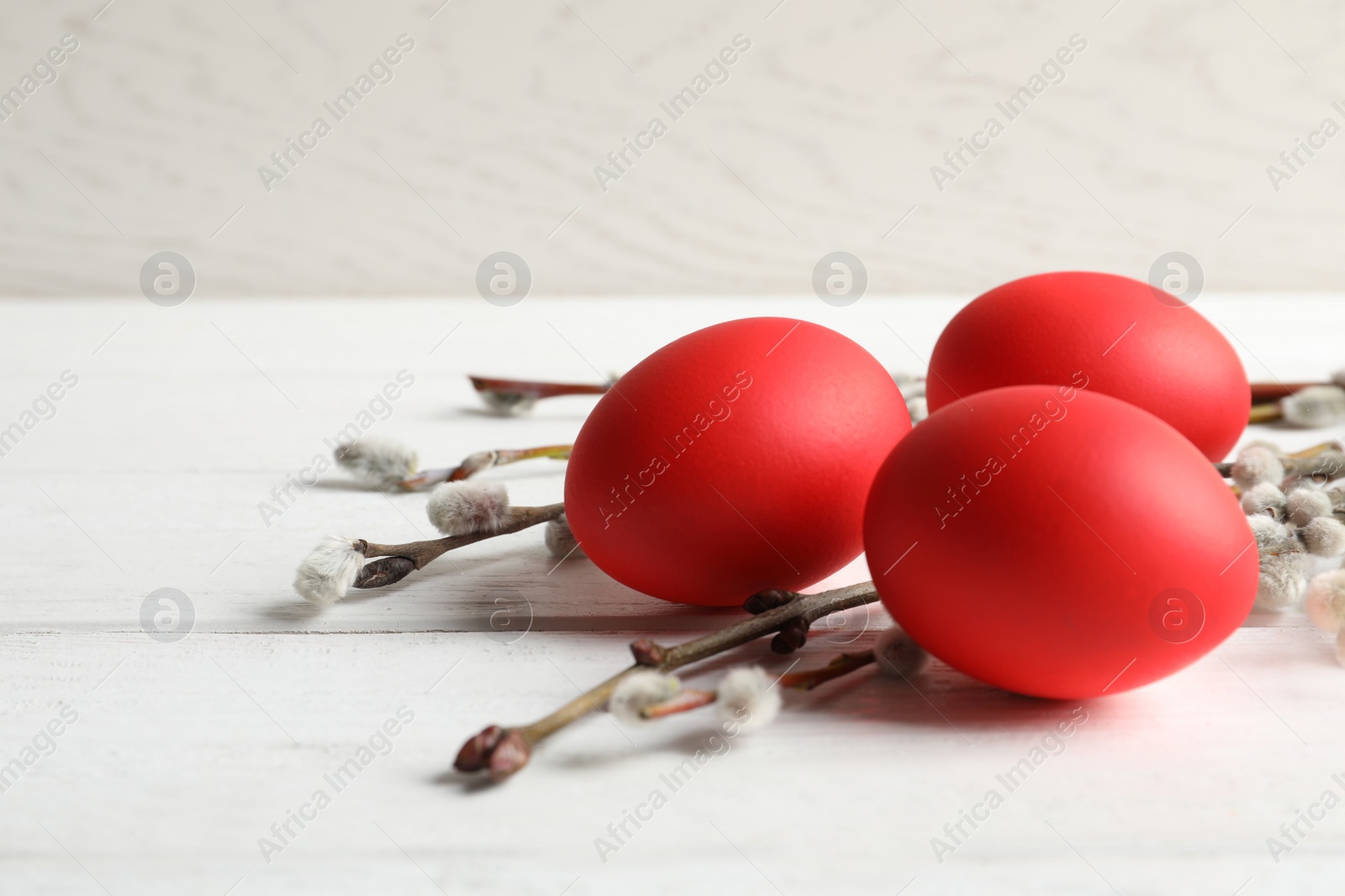 Photo of Red dyed Easter eggs and pussy willow on wooden table against light background, space for text