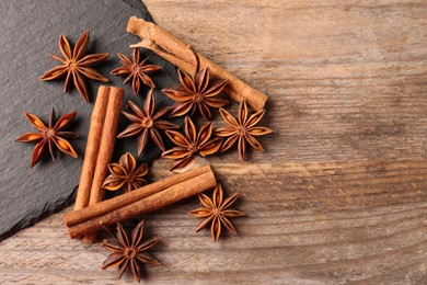 Aromatic cinnamon sticks and anise stars on wooden table, flat lay. Space for text