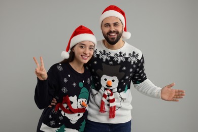 Photo of Happy young couple in Christmas sweaters and Santa hats on grey background