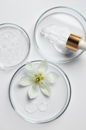 Photo of Petri dishes with samples of cosmetic oil, pipette and beautiful flower on white background, flat lay