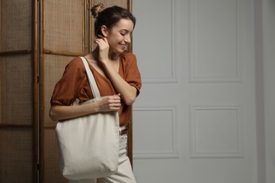 Photo of Happy young woman with blank eco friendly bag indoors. Space for text