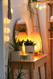 Photo of Green plants, lamp and different accessories on wooden table indoors. Interior design