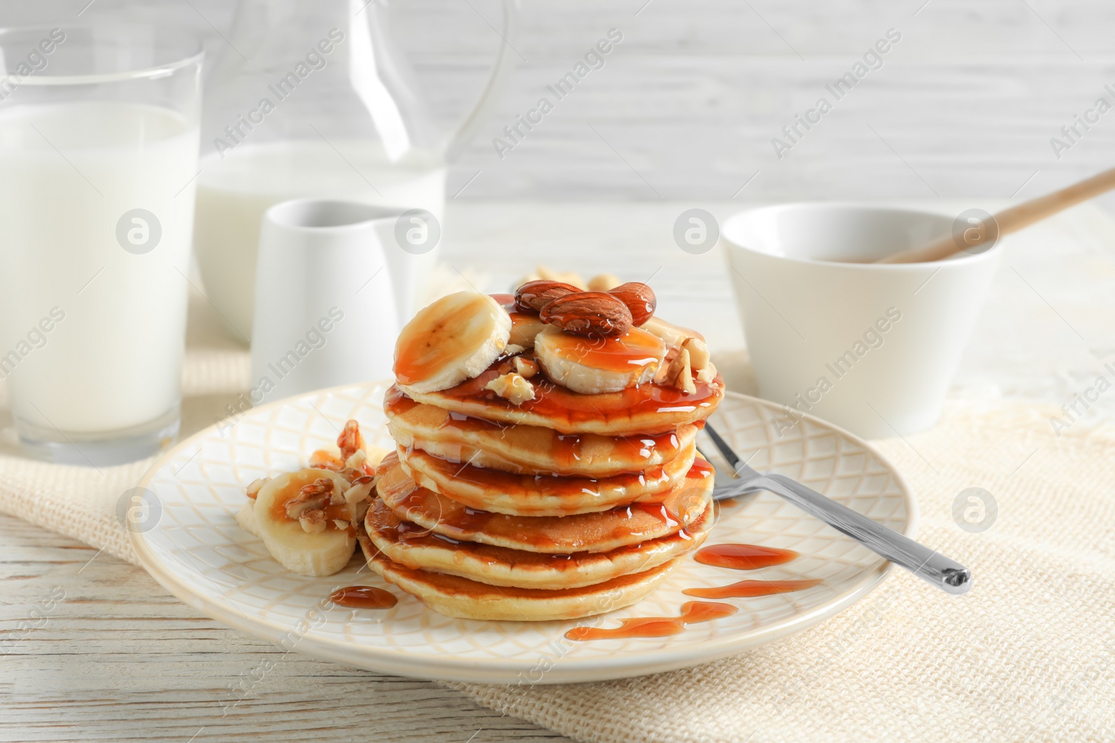 Photo of Stack of tasty pancakes with banana, nuts and syrup on table