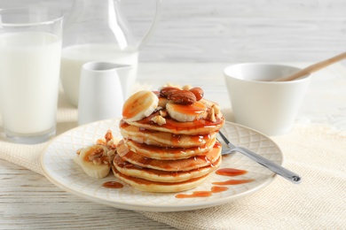 Stack of tasty pancakes with banana, nuts and syrup on table