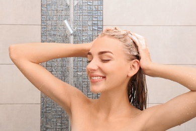 Beautiful young woman washing hair in shower at home