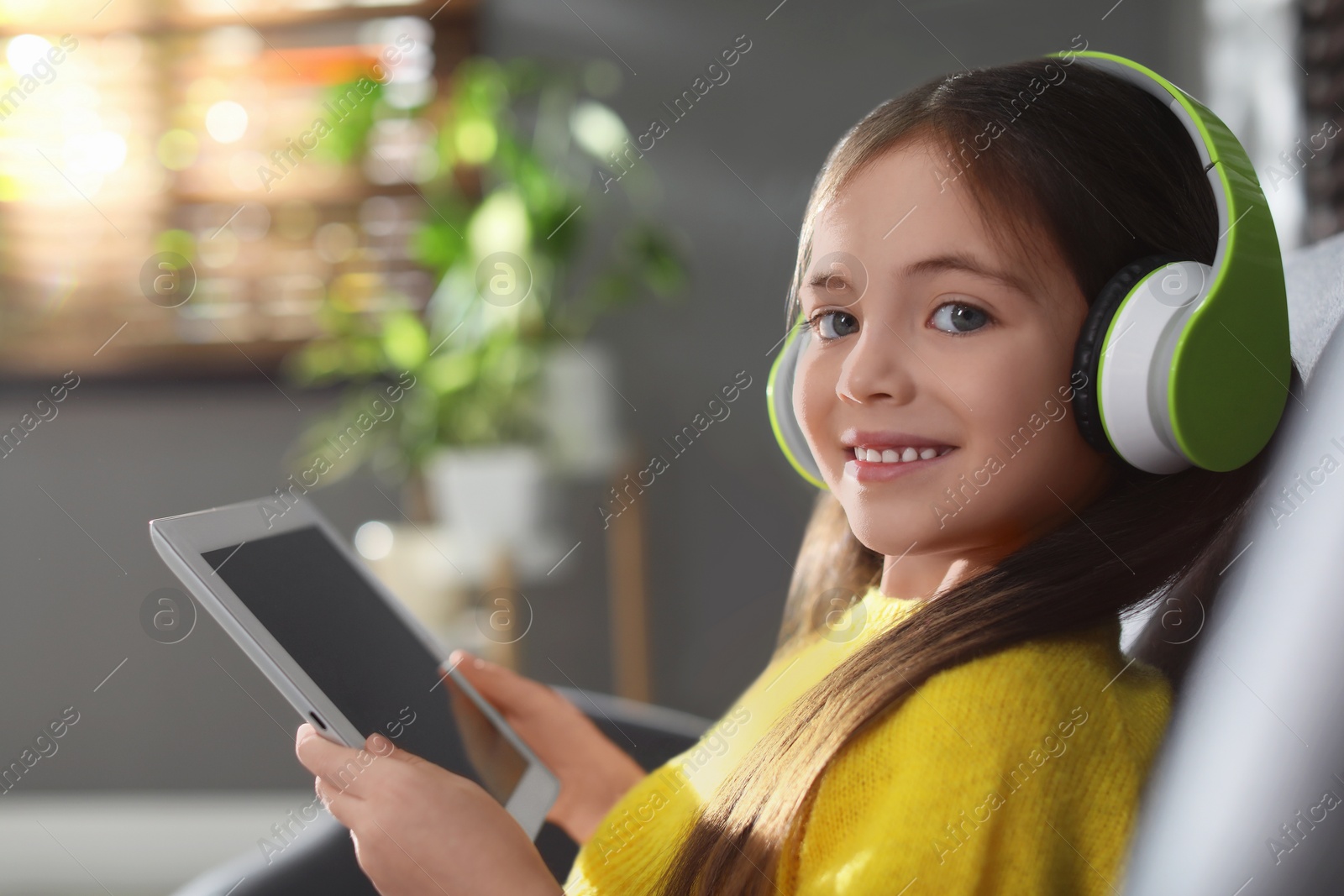 Photo of Cute little girl with headphones and tablet listening to audiobook at home