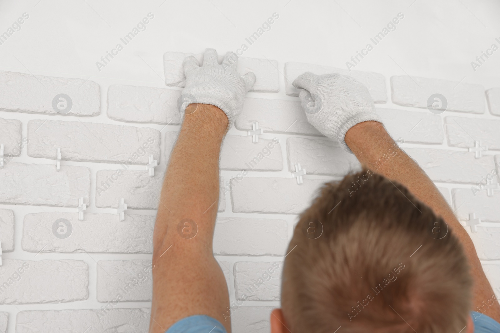 Photo of Professional builder installing new white decorative bricks on wall, closeup