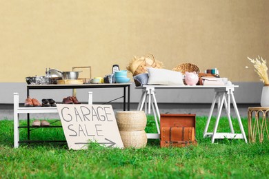 Photo of Sign Garage sale written on cardboard near tables with different stuff in yard