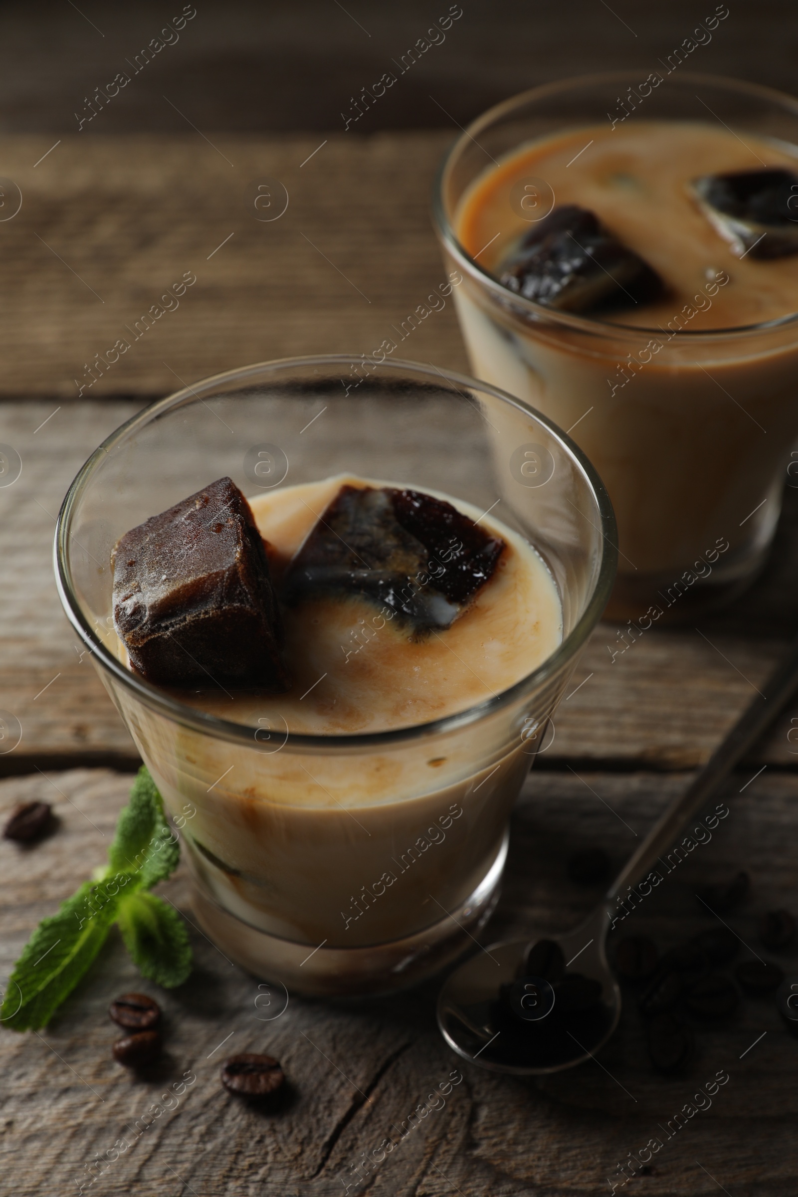 Photo of Glasses of delicious iced coffee with milk, beans and mint on wooden table