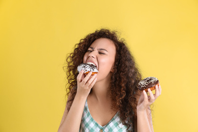 Photo of Beautiful African-American woman with donuts on yellow background