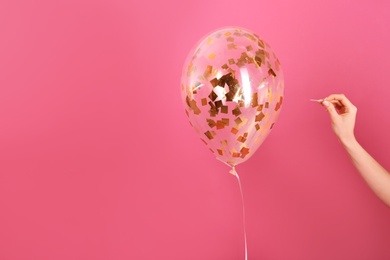 Photo of Woman piercing balloon with needle on color background, closeup. Space for text