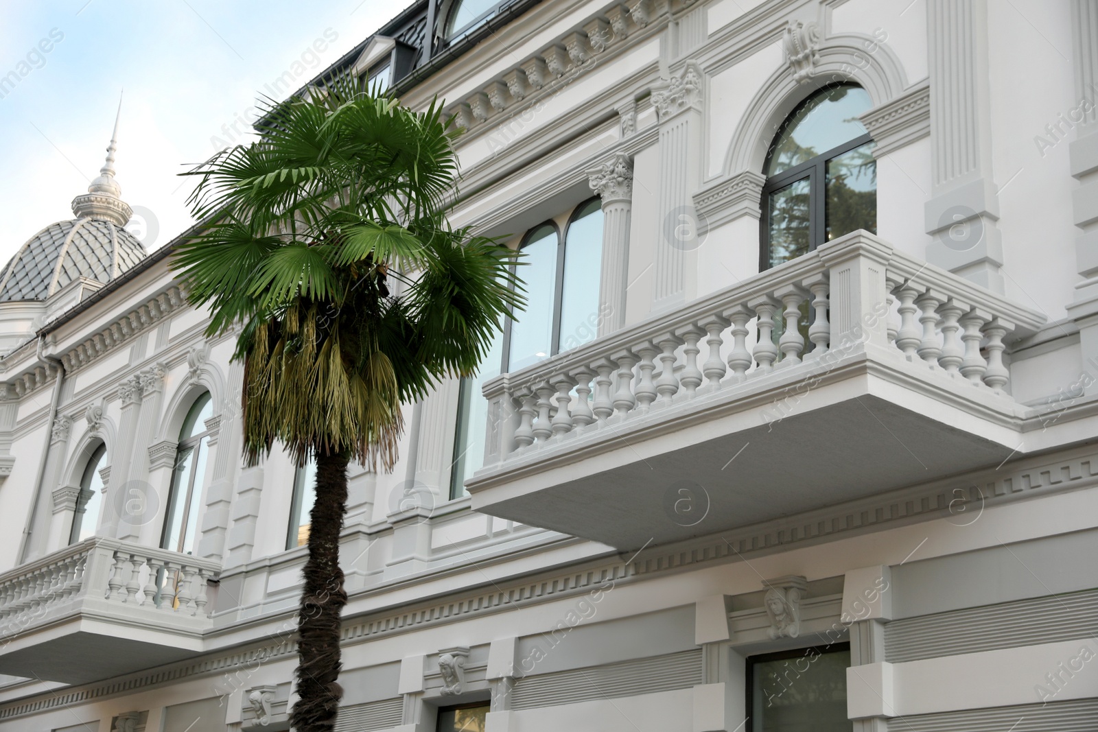 Photo of Exterior of beautiful building with balcony and palm tree outdoors