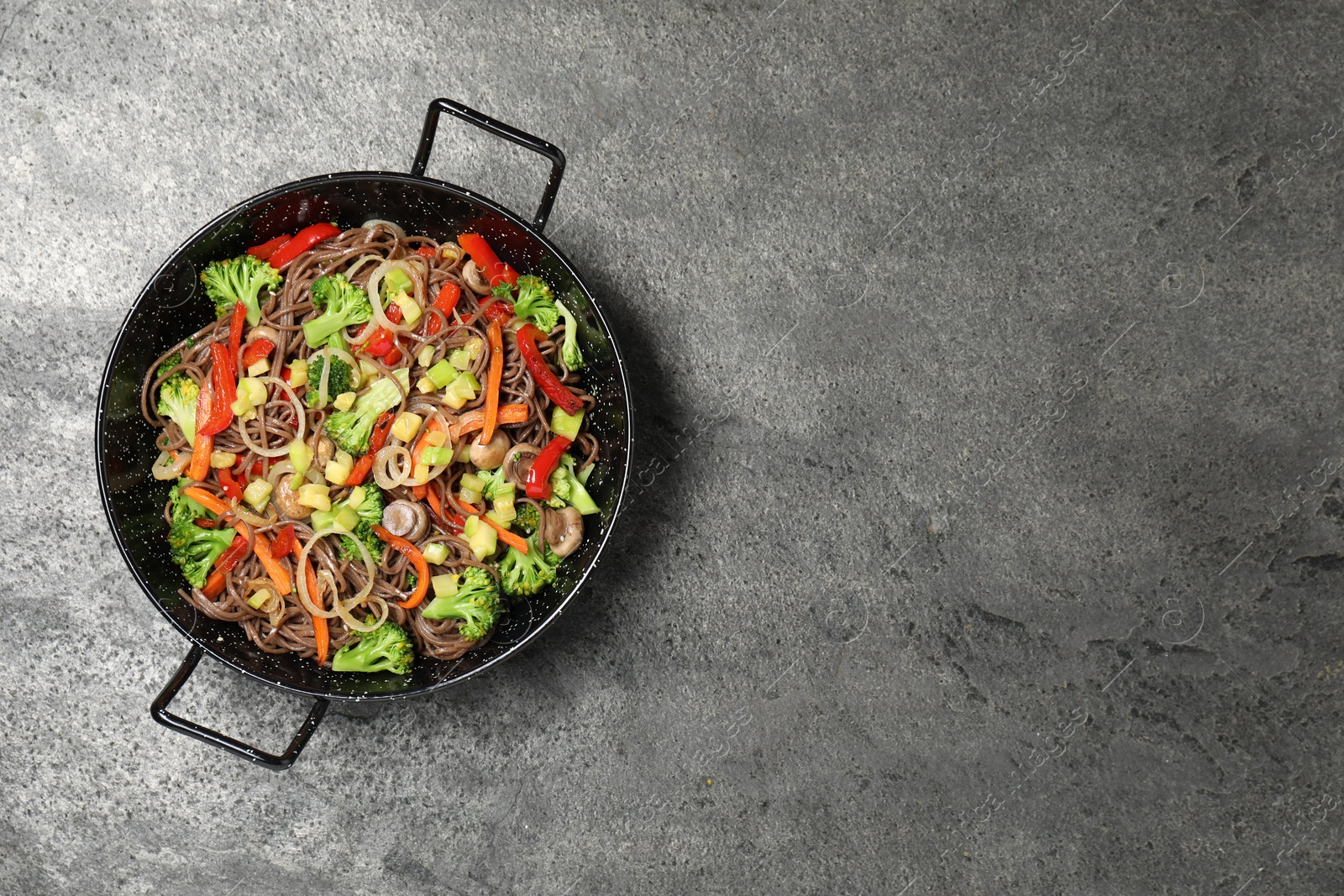 Photo of Stir fried noodles with mushrooms and vegetables in wok on grey table, top view. Space for text