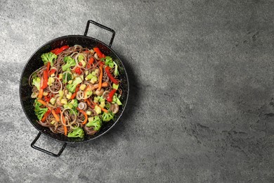 Stir fried noodles with mushrooms and vegetables in wok on grey table, top view. Space for text