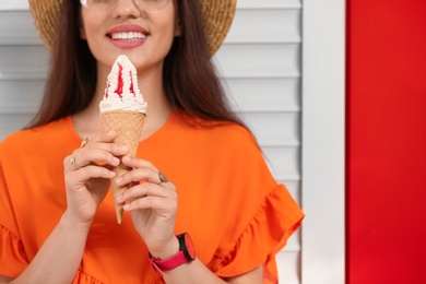 Photo of Happy young woman with delicious ice cream in waffle cone near color wall, closeup. Space for text