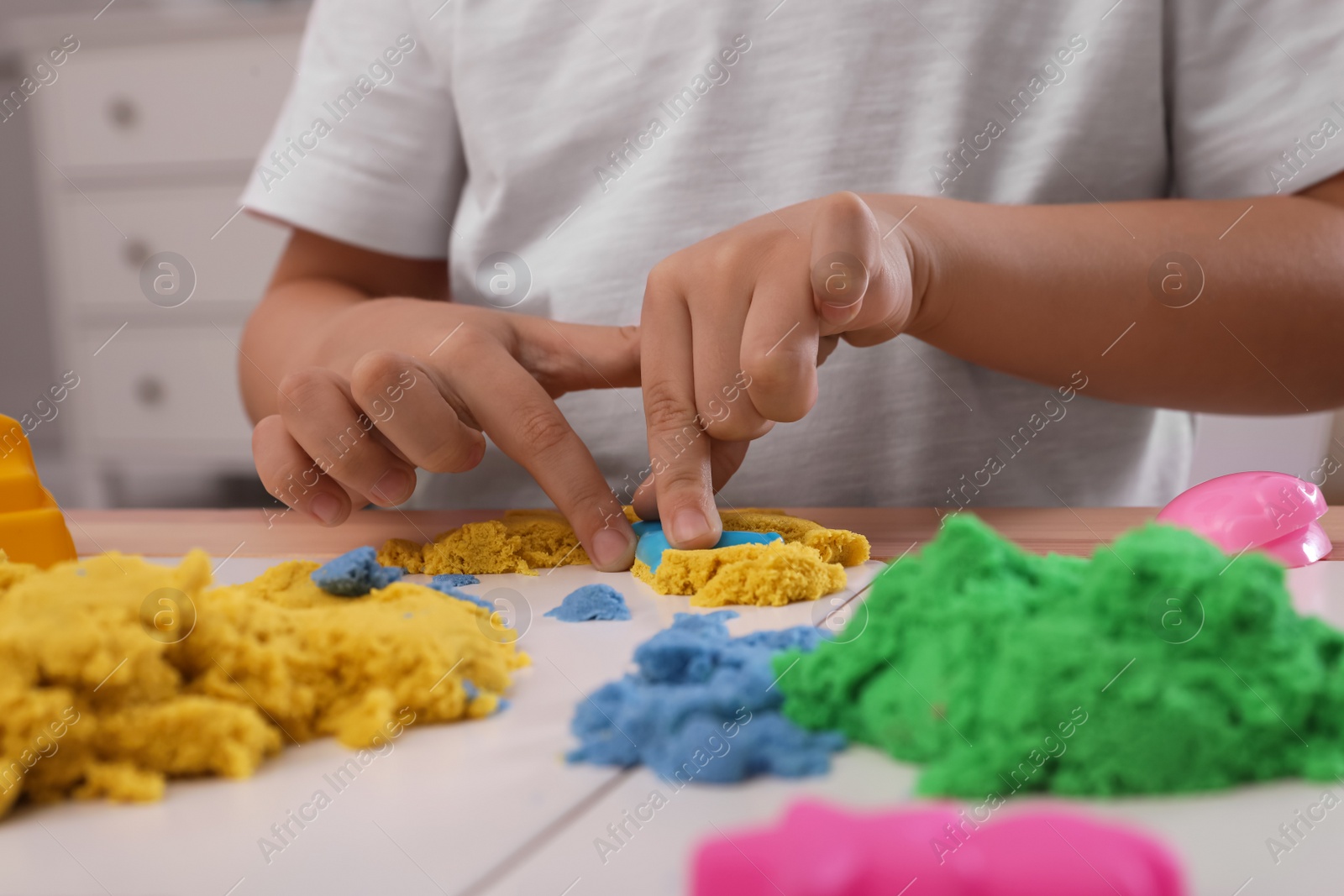 Photo of Little boy playing with bright kinetic sand at table indoors, closeup