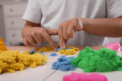 Little boy playing with bright kinetic sand at table indoors, closeup