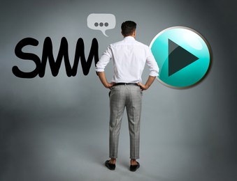 Image of Social media marketing. Man in business attire, abbreviation SMM and PLAY button icon on grey background
