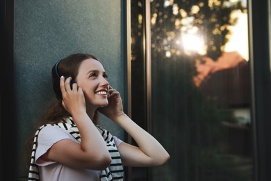 Photo of Happy woman in headphones enjoying music near building outdoors. Space for text