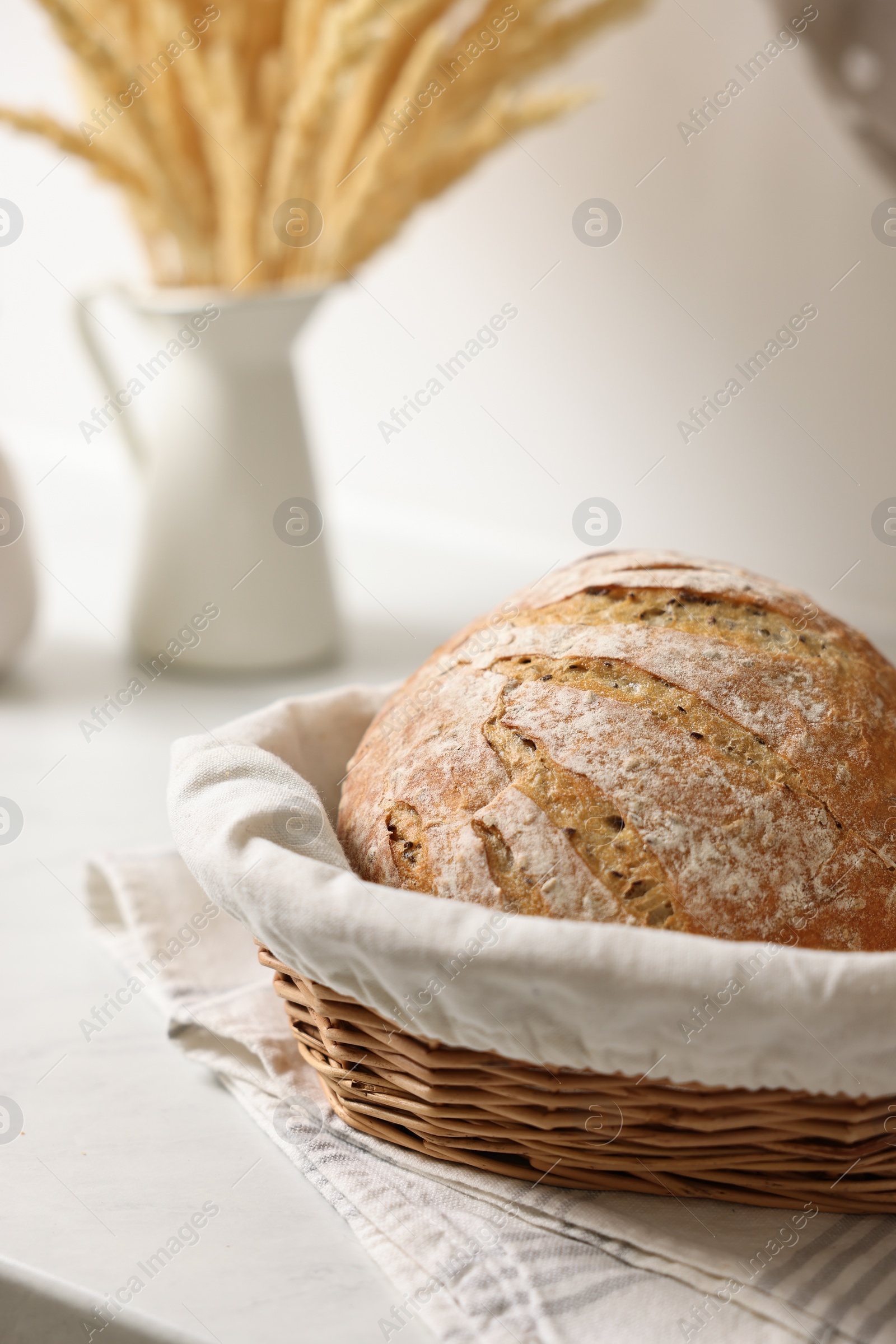 Photo of Wicker bread basket with freshly baked loaf on white marble table in kitchen, closeup