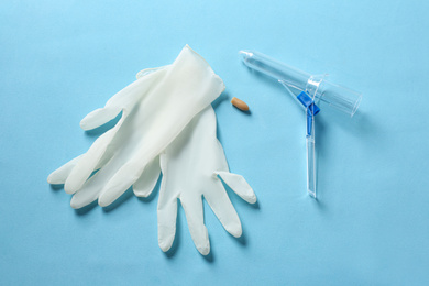 Photo of Anoscope, suppository and rubber gloves on light blue background, flat lay. Hemorrhoid treatment
