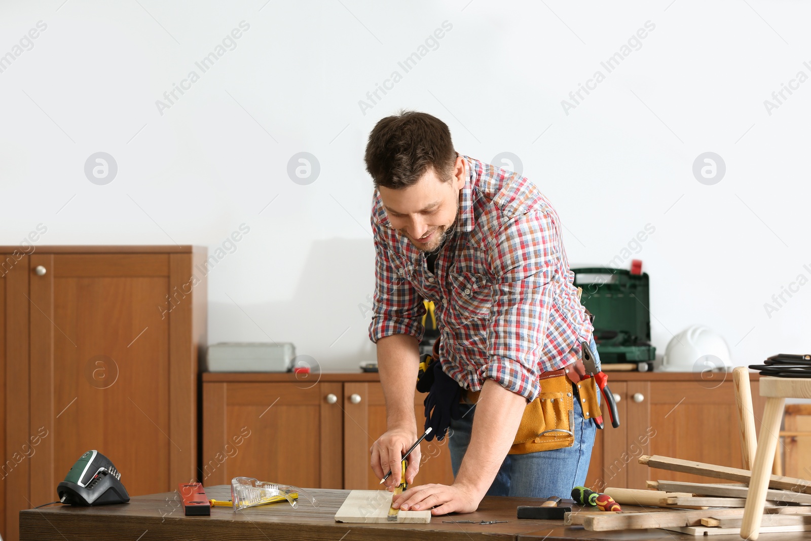 Photo of Handsome working man making marks on timber at table indoors. Home repair