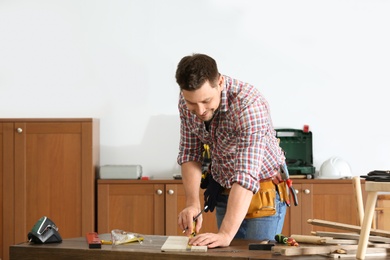 Photo of Handsome working man making marks on timber at table indoors. Home repair