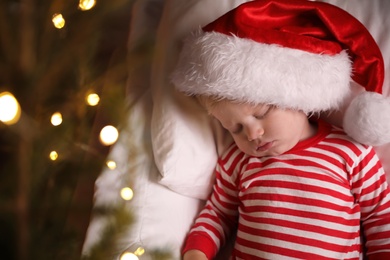 Photo of Baby in Christmas pajamas and Santa hat sleeping on bed, top view. Space for text