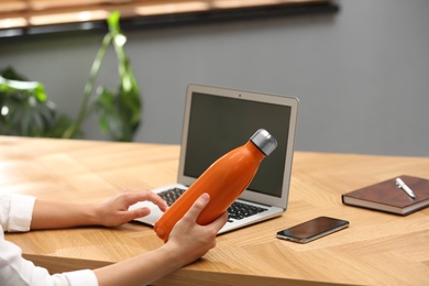 Photo of Woman with modern thermos bottle at workplace, closeup