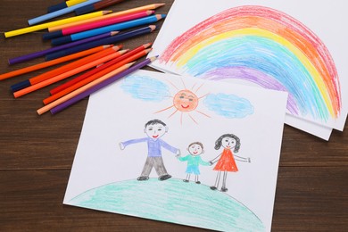 Photo of Cute child`s drawings and colorful pencils on wooden table, flat lay
