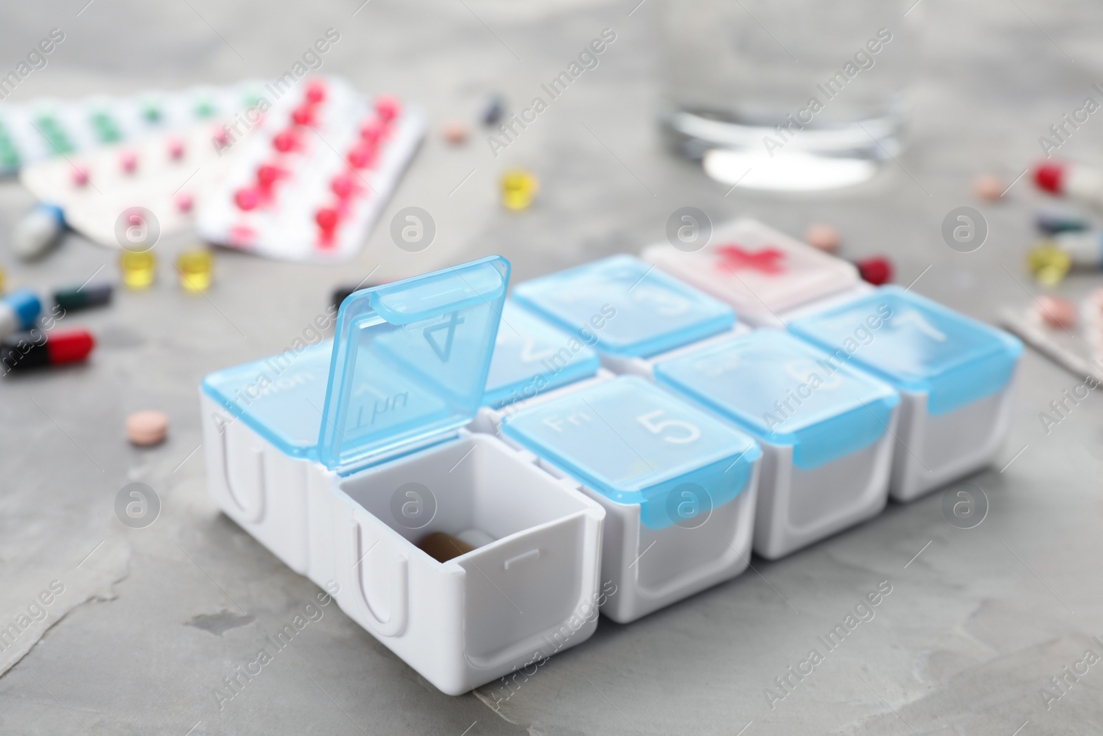 Photo of Plastic box with different pills on light grey stone table, closeup