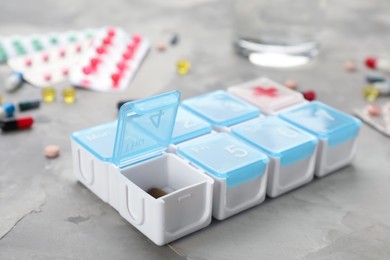 Photo of Plastic box with different pills on light grey stone table, closeup
