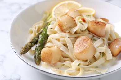 Photo of Delicious scallop pasta with asparagus and lemon on white table, closeup