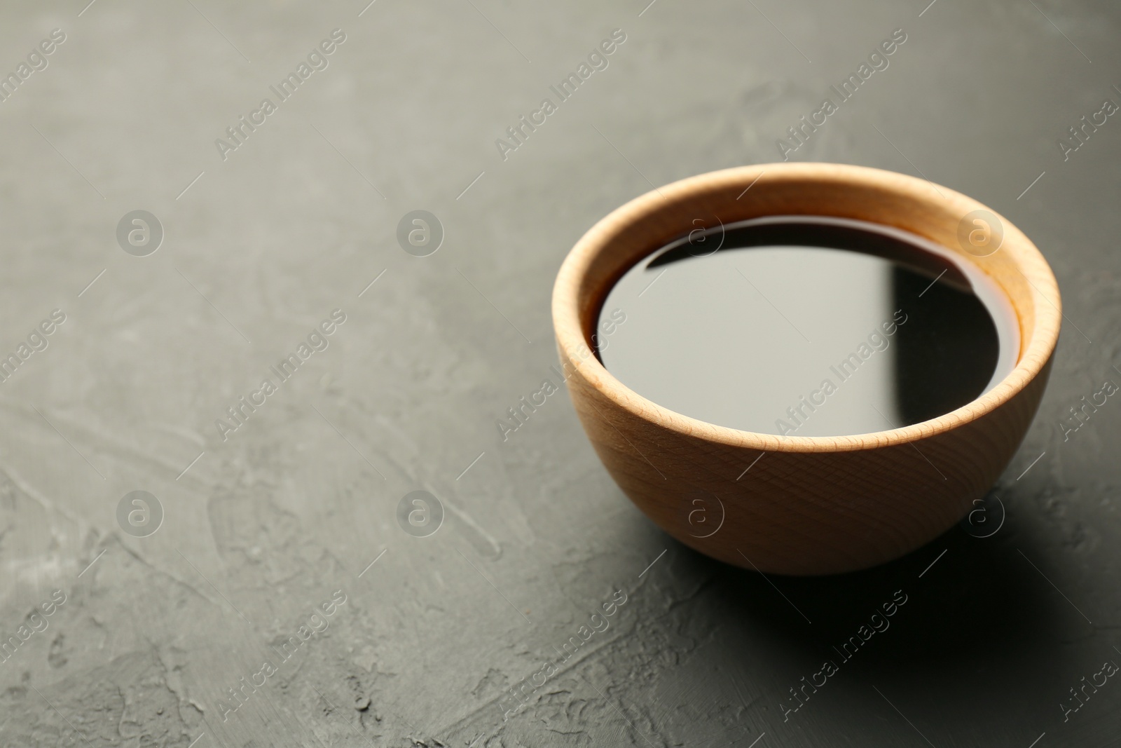 Photo of Soy sauce in wooden bowl on black textured table. Space for text