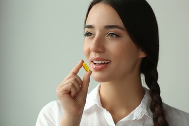 Young woman taking dietary supplement pill on grey background, space for text