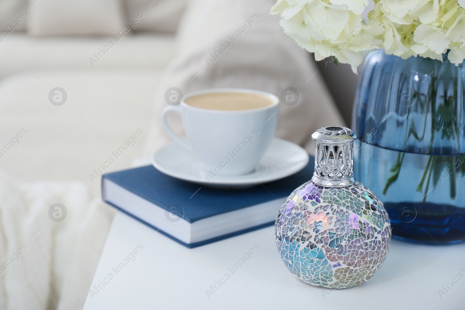 Photo of Stylish catalytic lamp with cup of coffee, book and flower on white table in living room. Cozy interior