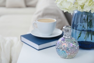 Photo of Stylish catalytic lamp with cup of coffee, book and flower on white table in living room. Cozy interior