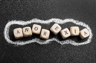 Photo of Word Anorexia made of wooden cubes on blackboard, flat lay
