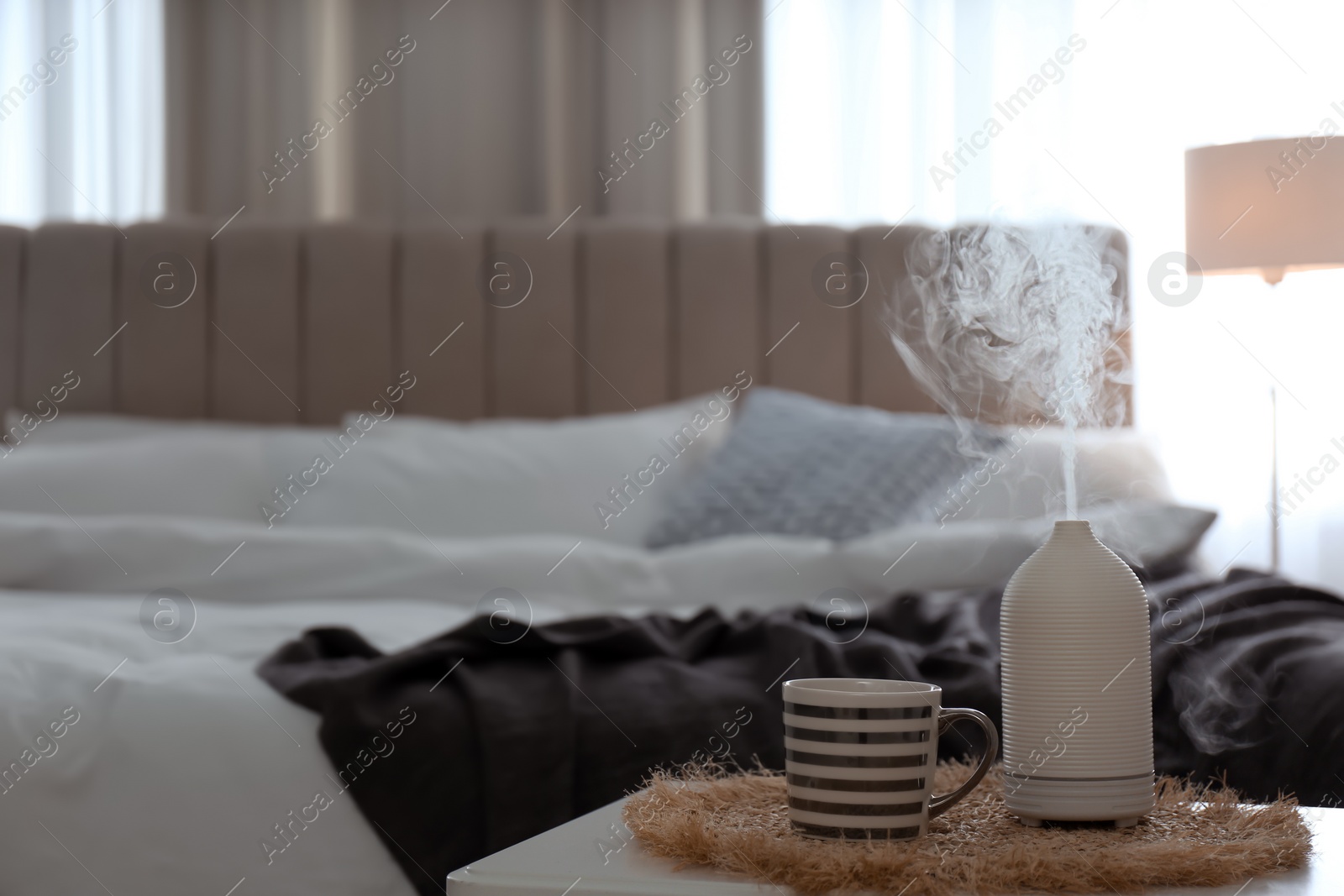 Photo of Aroma oil diffuser and cup of tea on table in bedroom. Space for text