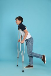 Teenage boy with injured leg using crutches on turquoise background