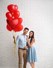 Photo of Young couple with air balloons near white brick wall. Celebration of Saint Valentine's Day