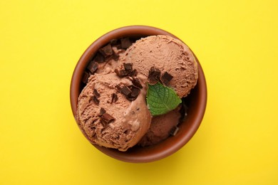 Photo of Bowl of tasty ice cream with chocolate chunks and mint on yellow background, top view