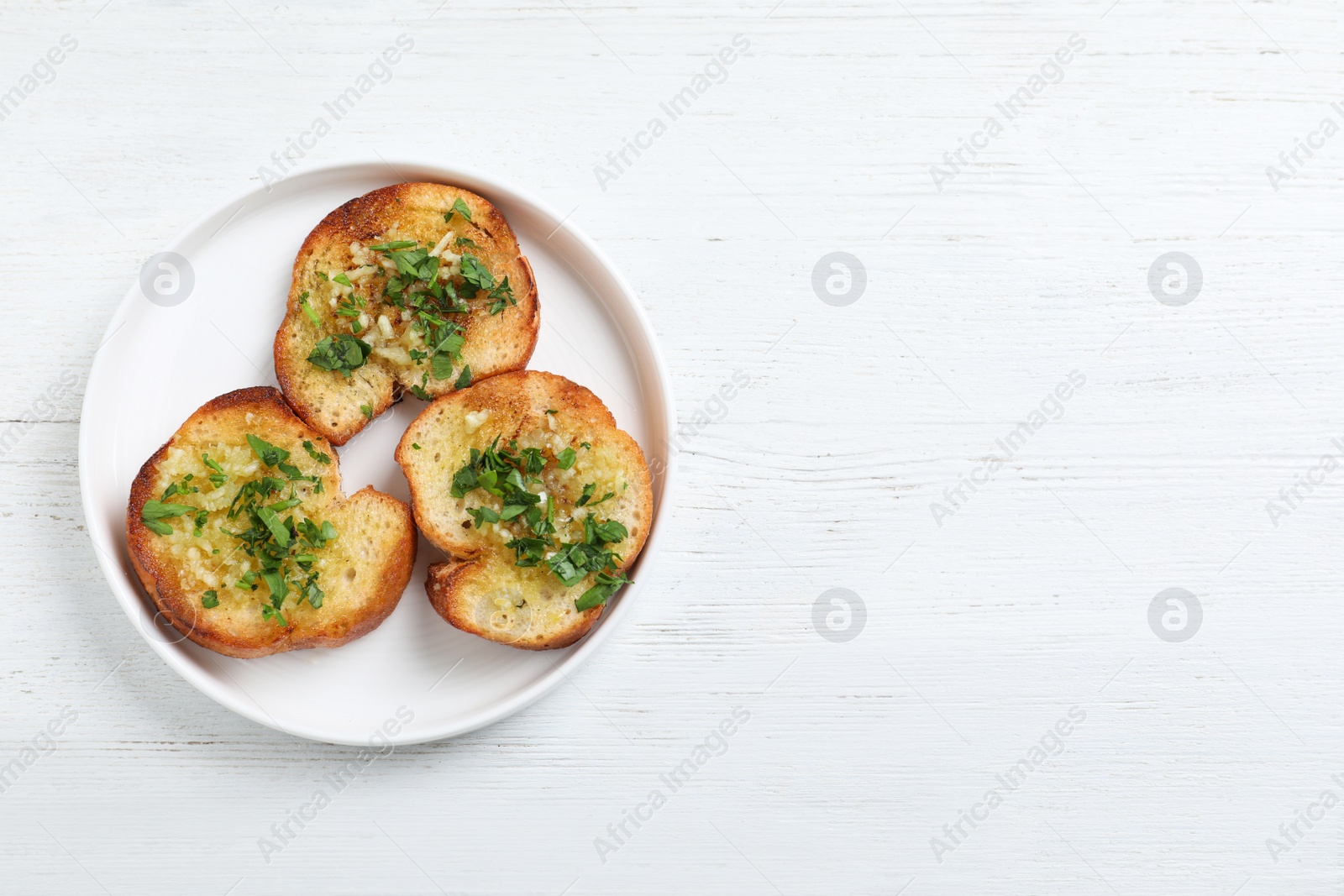 Photo of Slices of toasted bread with garlic and herb on white wooden table, top view. Space for text